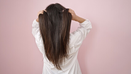 Young beautiful hispanic woman combing hair with hands over isolated pink background