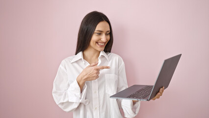 Young beautiful hispanic woman smiling confident pointing to laptop over isolated pink background