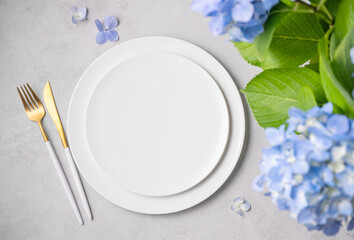 Festive table setting for spring celebration of women's day, birthday or mother's day with blue hydrangea flowers and white plates on a light background. Restaurant menu concept.