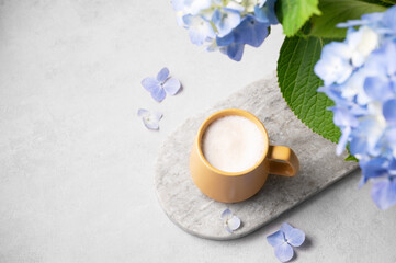 Spring bouquet with blue hydrangea flowers and a cup of cappuccino coffee in a yellow cup on a light background. The concept of a morning drink for breakfast.