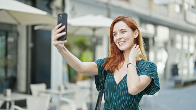 Young redhead woman smiling confident making selfie by the smartphone at coffee shop terrace