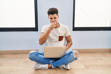 Young hispanic man using laptop at home feeling unwell and coughing as symptom for cold or...