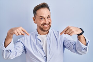 Middle age caucasian man standing over blue background looking confident with smile on face, pointing oneself with fingers proud and happy.