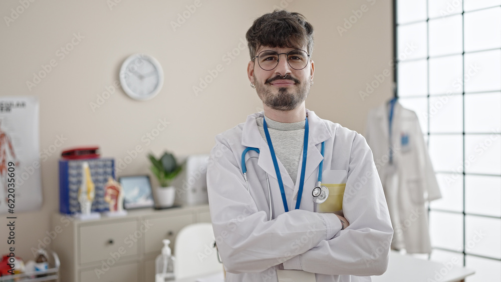 Wall mural young hispanic man doctor smiling confident standing with crossed arms at clinic