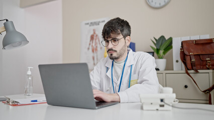 Fototapeta premium Young hispanic man doctor using laptop working at clinic