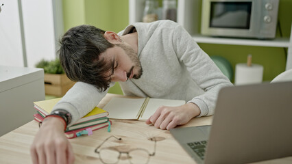 Young hispanic man writing notes tired at dinning room