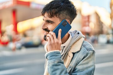 Young hispanic man talking on the smartphone wearing headphones at street