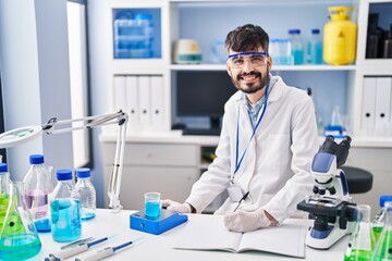 Young hispanic man scientist writing on notebook measuring liquid at laboratory