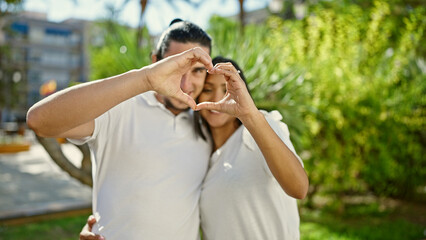 Man and woman couple standing together doing heart gesture at park