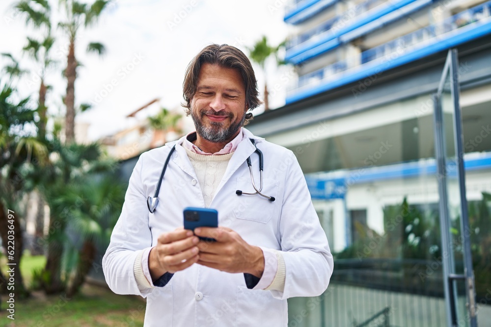 Canvas Prints Middle age man doctor smiling confident using smartphone at hospital