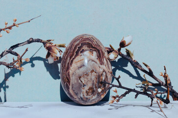 Easter egg with natural brown stone texture on blue background Spring still life with blooming tree branches white flowers. Cinematic vintage authentic Easter holiday concept photo. Springtime holiday