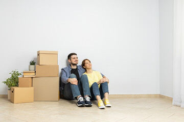 Fototapeta na wymiar A couple is sitting on the floor in an empty apartment, with boxes