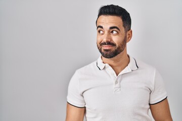 Young hispanic man with beard wearing casual clothes over white background smiling looking to the side and staring away thinking.