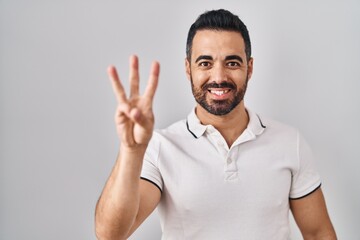 Young hispanic man with beard wearing casual clothes over white background showing and pointing up with fingers number three while smiling confident and happy.