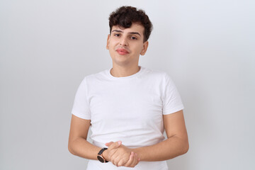 Young non binary man wearing casual white t shirt with hands together and crossed fingers smiling relaxed and cheerful. success and optimistic