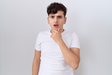 Young non binary man wearing casual white t shirt looking fascinated with disbelief, surprise and...