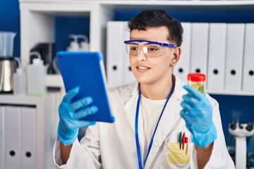 Young non binary man scientist holding urine test tube using touchpad at laboratory