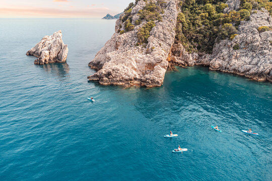 Aerial view of a group or team with paddles swims on a SUP boards on the sea near scenic rocks. Healthy lifestyle and recreation concept
