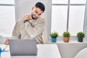 Young arab man suffering for back ache sitting on table working at home