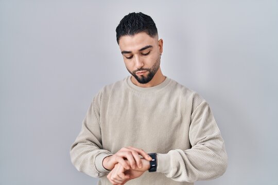 Young handsome man standing over isolated background checking the time on wrist watch, relaxed and confident