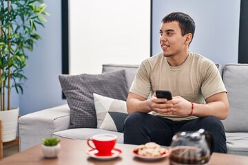 Young man having breakfast using smartphone at home