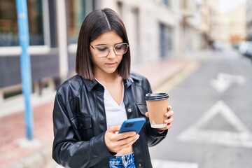 Young beautiful hispanic woman using smartphone driking coffee at street