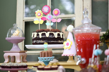 Um irresistível bolo de chocolate ao leite, com deliciosa cobertura de chocolate branco, decorado com encantadoras flores de papel, embelezando uma festa infantil cheia de alegria e diversão.
