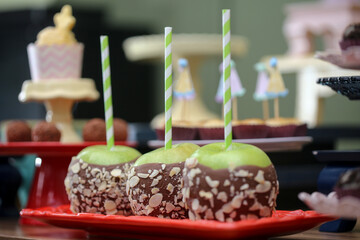 Maçãs do amor irresistíveis em uma versão especial, com maçãs verdes cobertas até a metade com chocolate e crocante de pistache, fazendo sucesso em uma animada festa infantil.