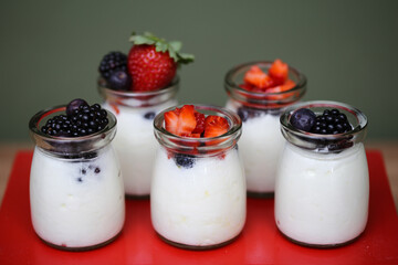Deliciosos potinhos de vidro com iogurte natural coberto com frutas vermelhas, uma opção refrescante e saudável para aproveitar em eventos descontraídos.