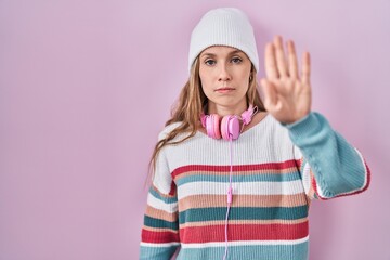 Young blonde woman standing over pink background doing stop sing with palm of the hand. warning expression with negative and serious gesture on the face.