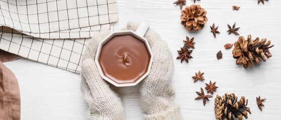 Fototapeta na wymiar Female hands with cup of hot chocolate and cones on white wooden background, top view