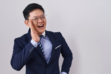 Young asian man wearing business suit and tie shouting and screaming loud to side with hand on mouth. communication concept.
