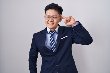 Young asian man wearing business suit and tie smiling pointing to head with one finger, great idea or thought, good memory