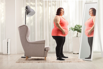 Overweight woman holding her belly in front of mirror at home