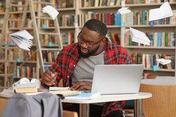 African-American student preparing for exam in library with flying books