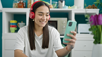 Young beautiful hispanic woman listening to music sitting on table at dinning room