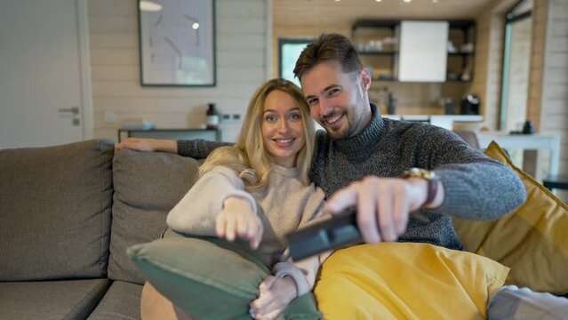 TV POV of joyful couple switching channels with remote control talking laughing. Front view positive Caucasian adult boyfriend and girlfriend enjoying weekend leisure together on couch in living room