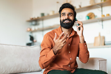 Cheerful Handsome Arab Guy Talking On Cellphone In Living Room