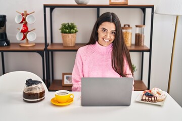 Young hispanic woman using laptop having breakfast at home