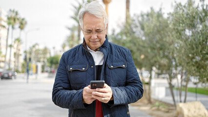 Fototapeta premium Middle age man with grey hair using smartphone at park