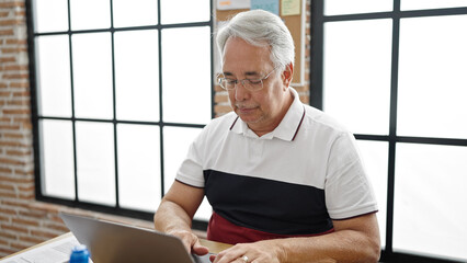 Middle age man with grey hair business worker using laptop with serious face at office