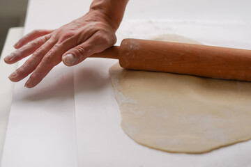 Close-up of rolling thin dough. The process of making dough for Ukrainian dumplings and other dough recipes. Beautiful view with a hand of raw homemade rolled dough on a light background