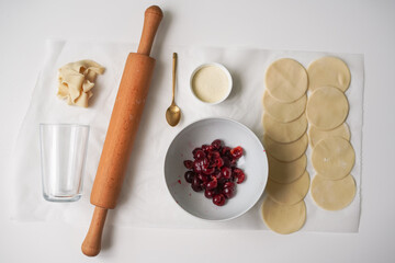 Traditional Ukrainian recipes. Round dough, sour cherry filling, rolling pin, spoon and other kitchen tools for making homemade Ukrainian varenyki