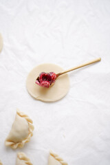 Homemade Ukrainian varenyki. A spoonful of cherries and raw dumpling dough on the background of the cooking process, raw varenyki