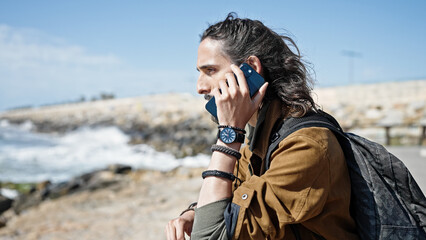 Young hispanic man tourist wearing backpack talking on smartphone at seaside