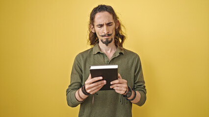 Young hispanic man reading book surprised over isolated yellow background