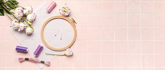 Embroidery hoop with canvas, threads, pins and flowers on pink tile background with space for text