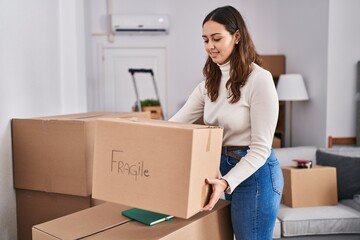 Young beautiful hispanic woman smiling confident holding fragile package at new home