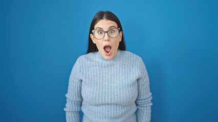 Young hispanic woman standing with surprise expression over isolated blue background