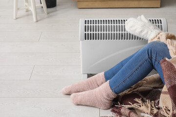 Woman in winter clothes warming near radiator at home, closeup